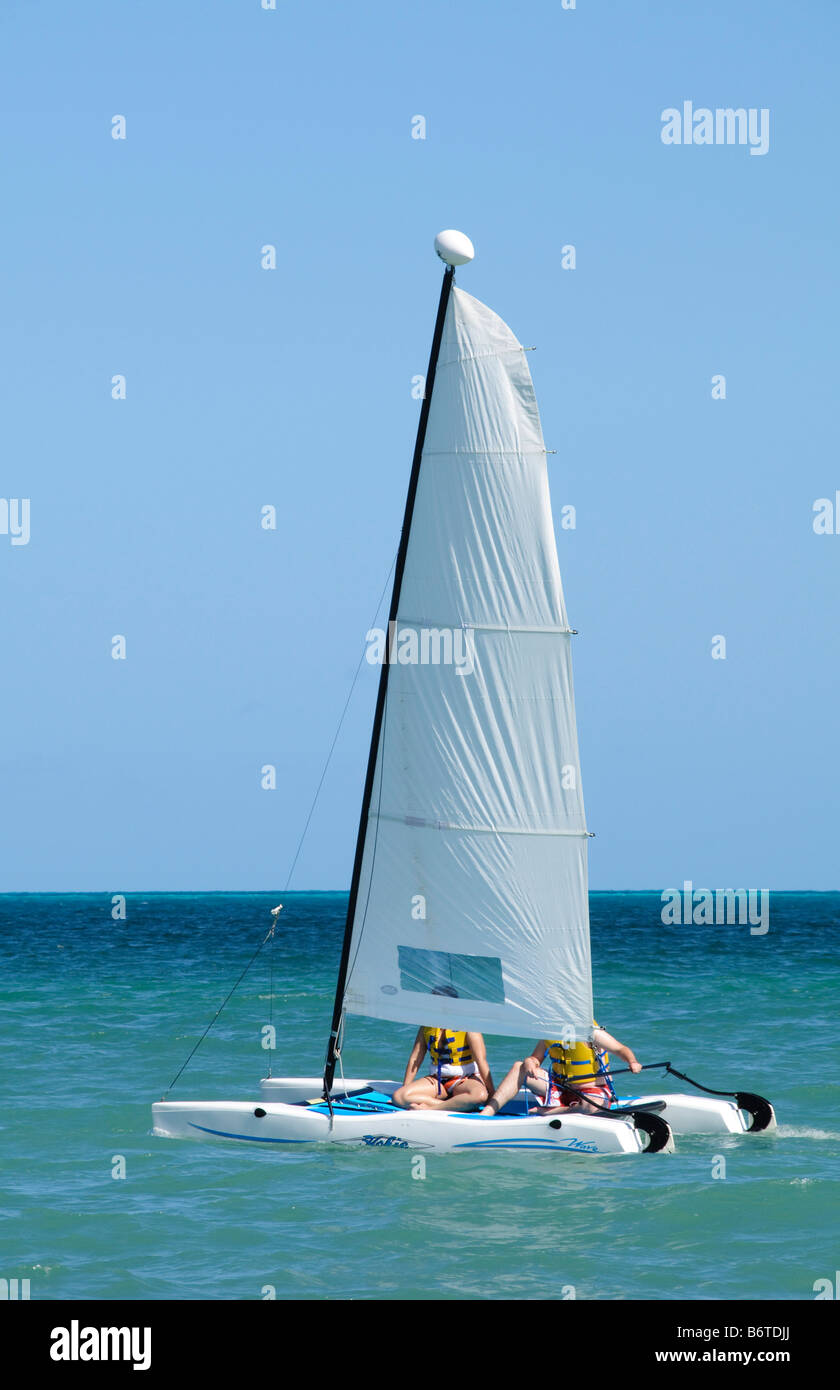 Hobie Cat Catamaran Segeln Playa Mujeres Mexiko // PLAYA MUJERES, Mexiko - Touristen segeln einen Hobie Cat Katamaran vor dem Strand in Playa Mujeres in Mexiko. Playa Mujeres liegt an der Nordküste der Halbinsel Yucatan, etwa 10 Kilometer nördlich von Cancun. Der Strand ist Teil des Entwicklungsgebiets Costa Mujeres, das zu einem beliebten Ziel für Urlaubstourismus und Wassersportaktivitäten geworden ist. Hobie Cat Katamarane werden aufgrund ihrer Stabilität und Bedienfreundlichkeit häufig für Freizeitsegel in Strandresorts in der Karibik und im Golf von Mexiko verwendet Stockfoto