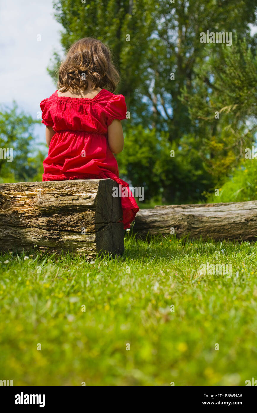 Ein Mädchen sitzt auf einem Baumstamm Stockfoto
