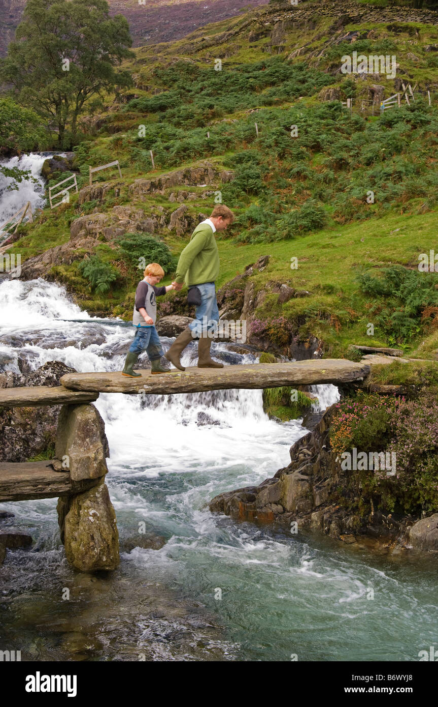 Wales, Conwy, Snowdonia. Man führt ein Junge über eine rustikale Brücke über Afon Cwm Llan auf der Strecke in Snowdon Stockfoto