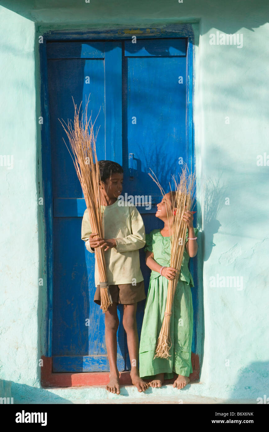 Zwei Kinder stehen mit Besen vor einer Tür, Hampi, Karnataka, Indien Stockfoto