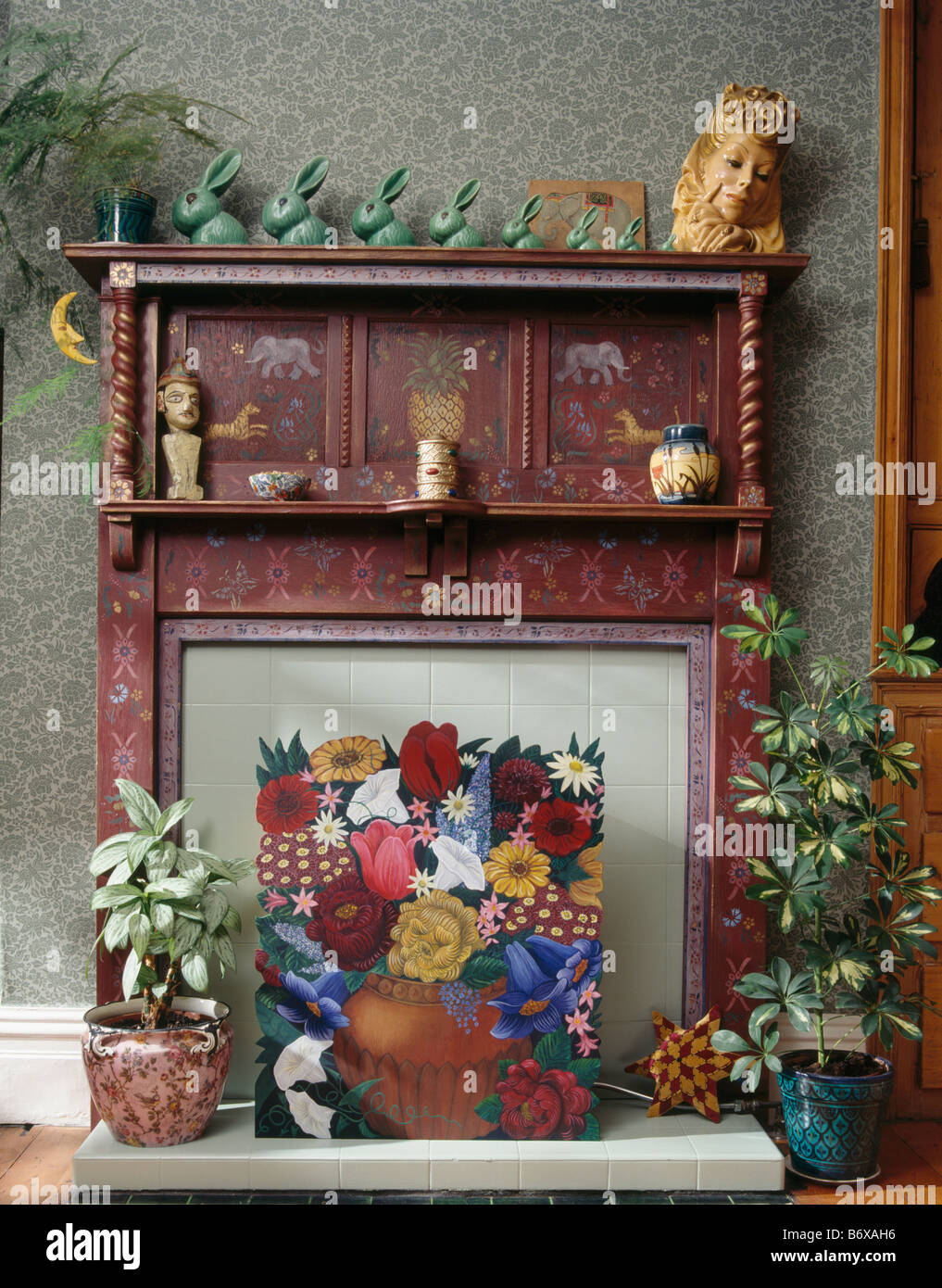 Zimmerpflanzen und gemalte Blumen FUNKENSCHUTZGITTER vor malte dreißiger Jahre Kamin mit Sammlung von grünen Denby Kaninchen Stockfoto
