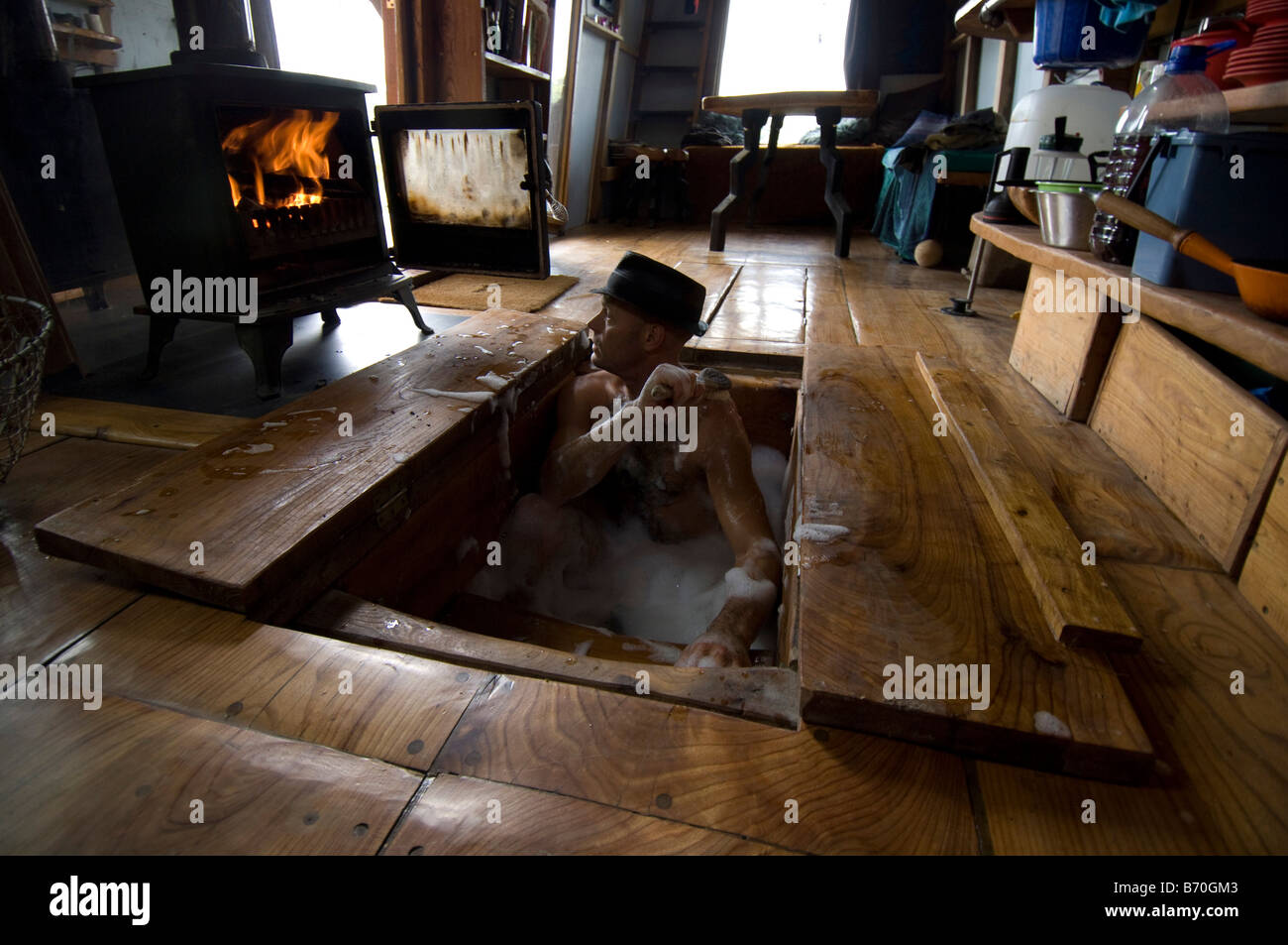 Mann baden in seine Hand aus Holz Kabine, in der Badewanne, unter der Küche, Boden und Wasser erhitzt auf Holz befeuerten Herd eingestellt ist. Off Grid leben. Stockfoto