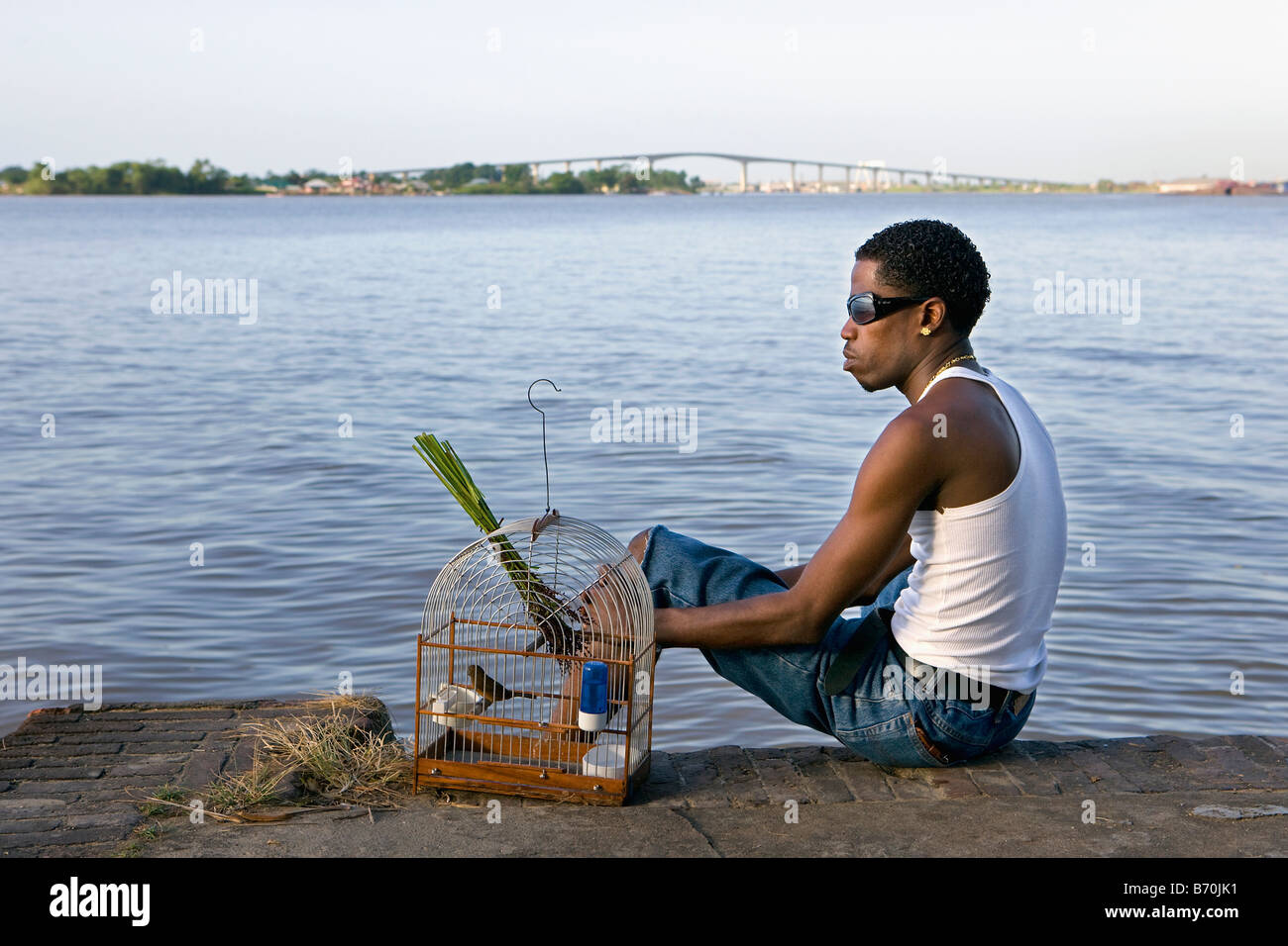 Suriname, Paramaribo. Kreolische Mann und Picolet Singvogel, essen Reis-Rasen. Suriname-Fluss und Wijdenbosch Brücke. Stockfoto