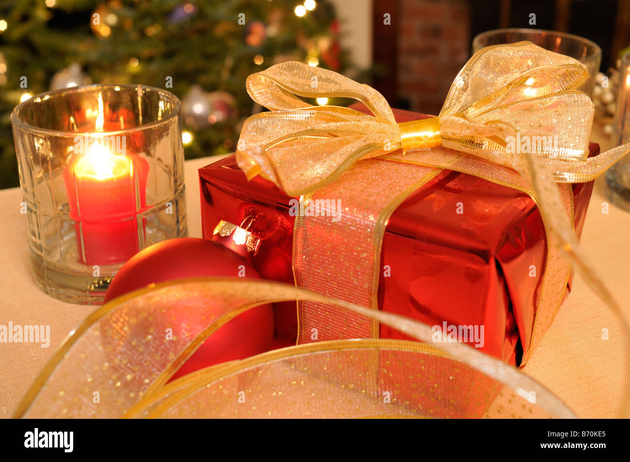 Geschenk verpackt rot Weihnachtsgeschenk mit Flitter beleuchteten Baum Kerzen und Gold Ribbon auf Tisch. Stockfoto