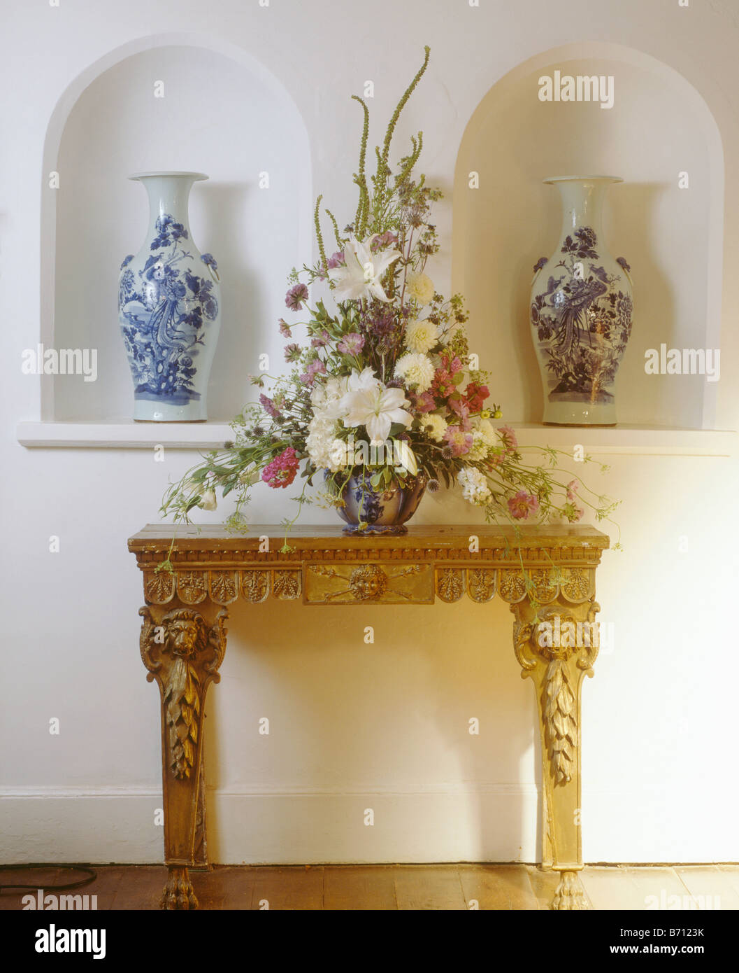 Weiße Lilien in Frisches Blumenarrangement auf Konsole Tisch vor Nischen mit hohen blaue und weiße Vasen Stockfoto