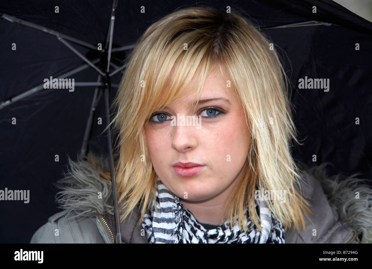 18 jährige Blondine mit schwarzen Regenschirm tragen Jacke und schwere Schal direkt in der Kamera Blickkontakt suchen Stockfoto