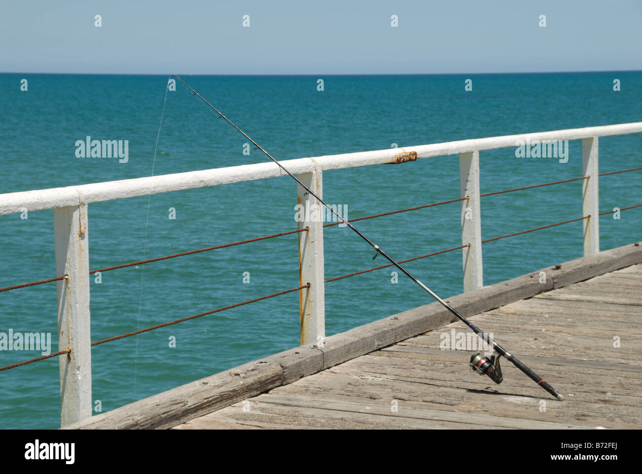 Eine Angelrute, die gegen die Schienen am Henley Steg gestützt, während ein Fischer ein knabbern Henley Beach Adelaide South Australia erwartet Stockfoto