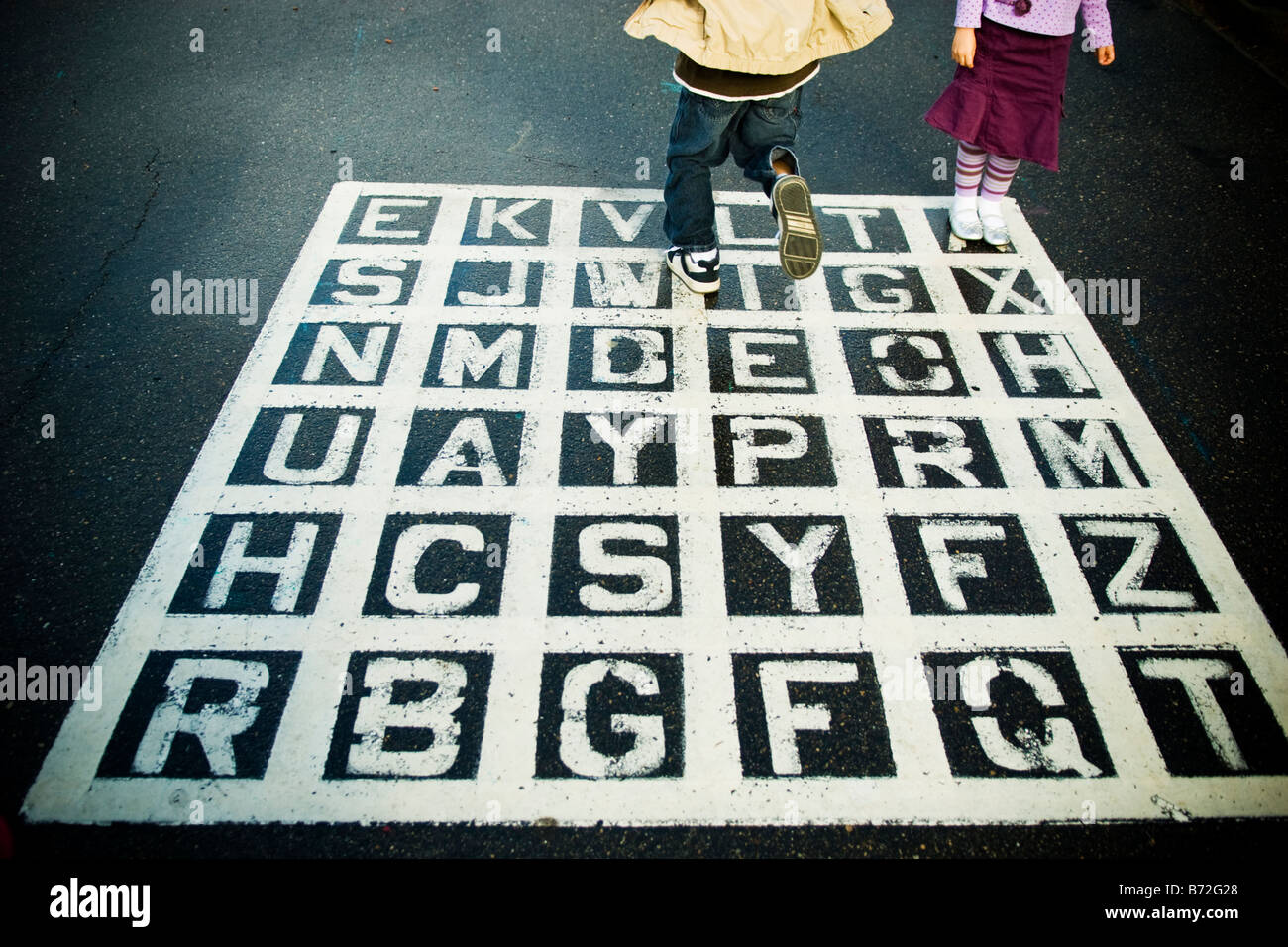 Kinder spielen auf einem Asphalt-Alphabet-Spiel auf dem Schulhof. Stockfoto