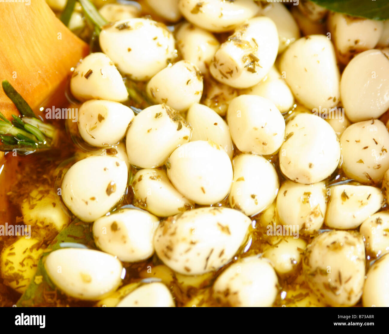 Nahaufnahme von Knoblauchzehen in Olivenöl und Kräutern mariniert, mit einem hölzernen Löffel auf einem Marktstand Stockfoto