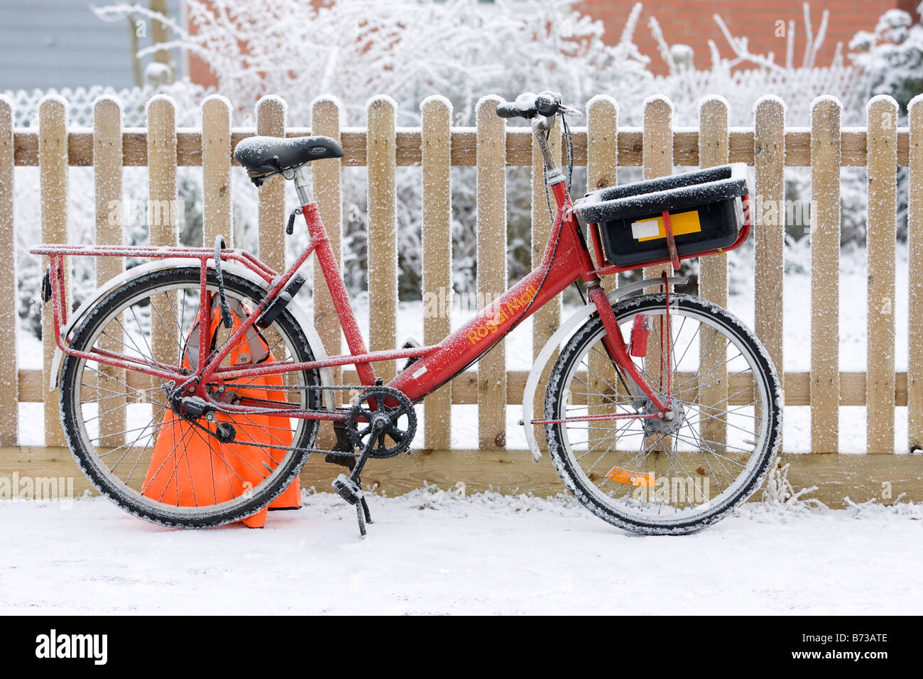 Eine britische Königliche Post Postversand Fahrrad an einem schneereichen Wintern Morgen gegen einen Zaun gelehnt. Stockfoto