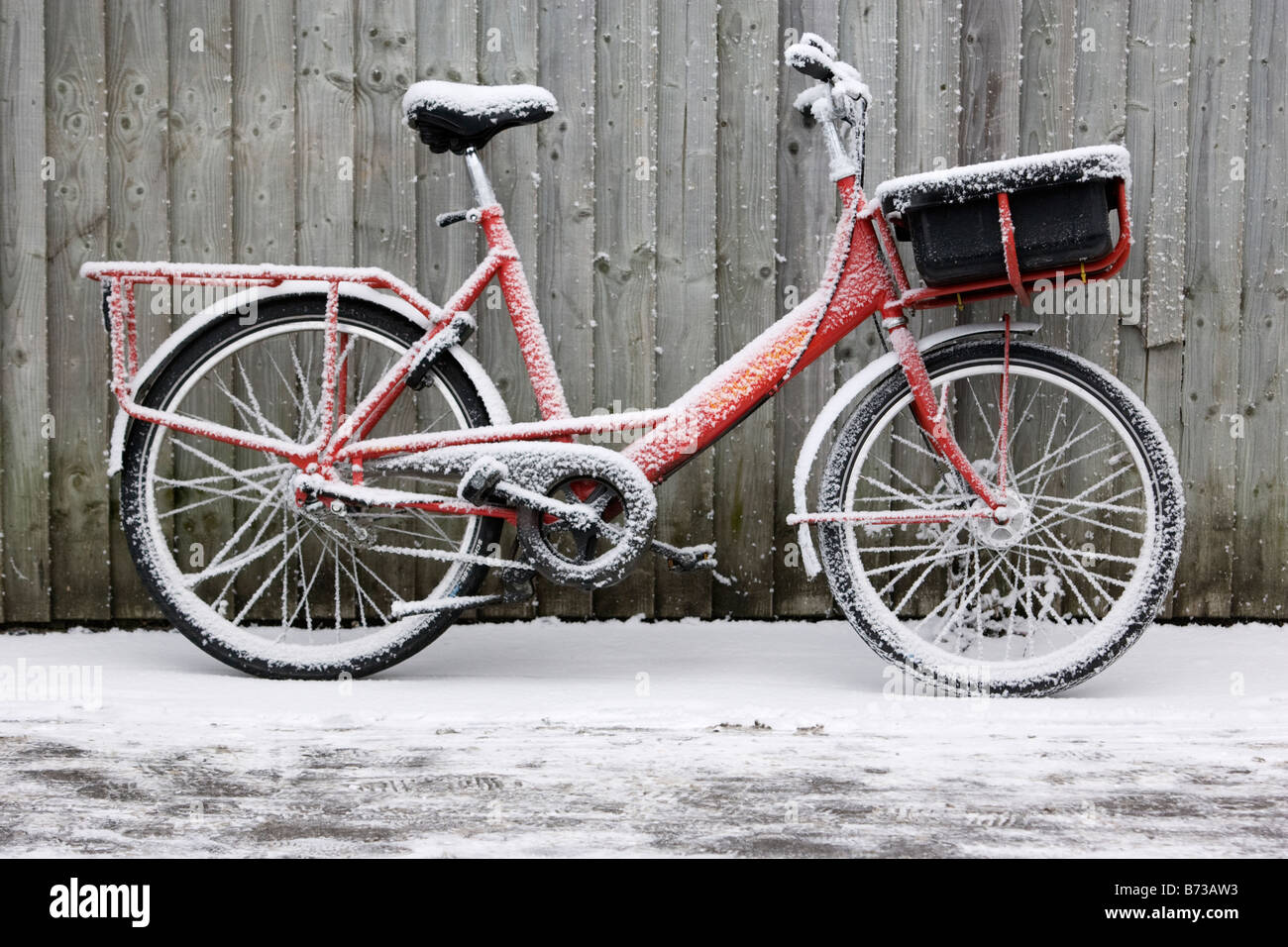 Eine britische Königliche Post Postversand Fahrrad an einem schneereichen Wintern Morgen gegen einen Zaun gelehnt Stockfoto