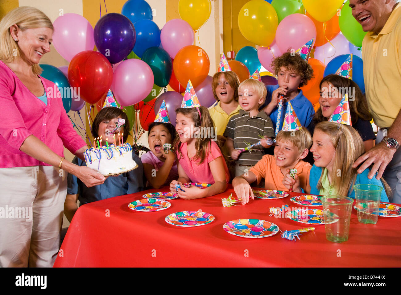 Gruppe von Kindern, die Spaß an der Geburtstagsfeier, Mutter hält Kuchen Stockfoto