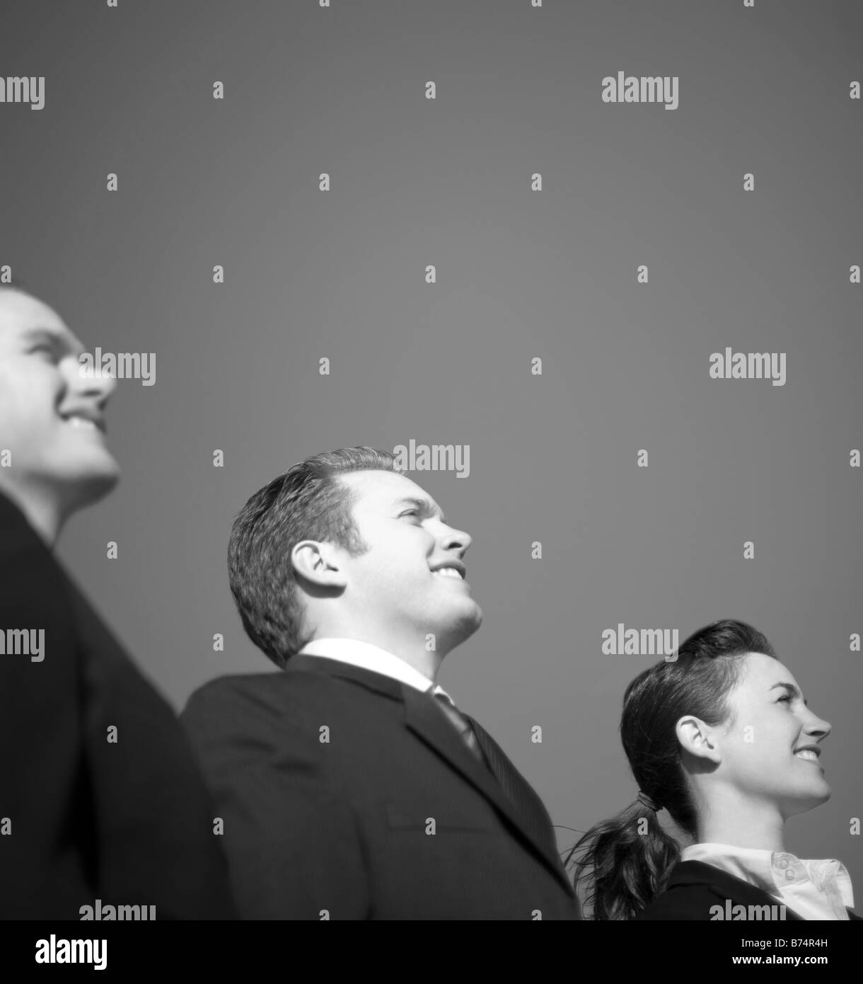 Drei Geschäftsleute in Anzüge stehen in einer Zeile lächelnd und blickte in die gleiche Richtung mit einem blauen Himmelshintergrund Stockfoto