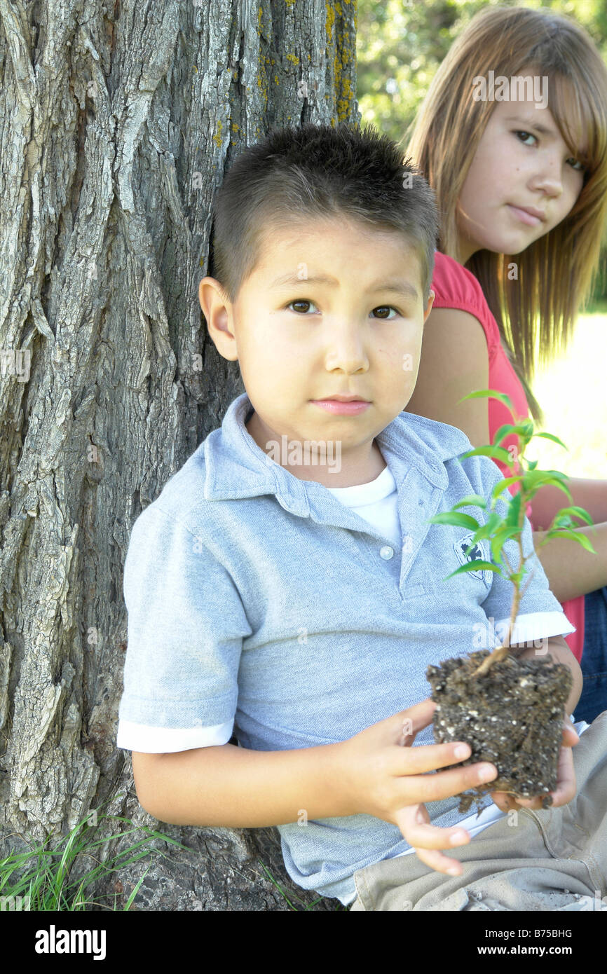 13 Jahre altes Mädchen und sechs Jahre alten Jungen mit kleiner Baum sitzend neben Baum, Winnipeg, Kanada Stockfoto