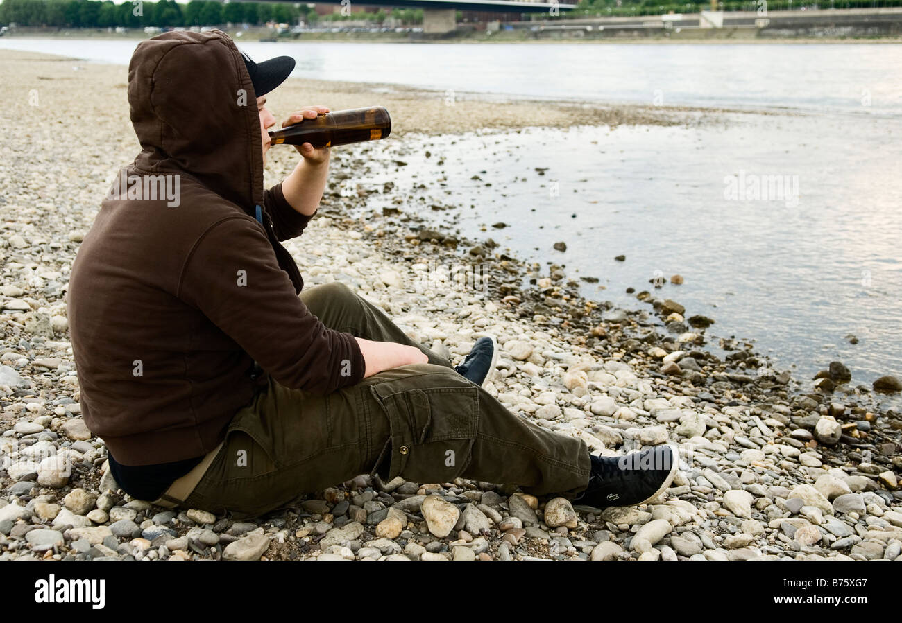 einsame junge sitzt am Ufer und eine Flasche Bier trinkt Stockfoto