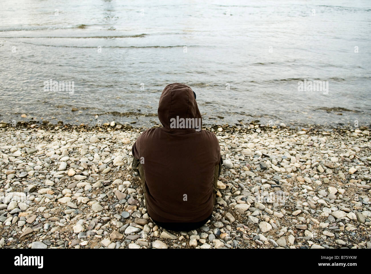 einsame junge sitzt am Ufer tragen braune Sweatshirt mit Kapuze Stockfoto