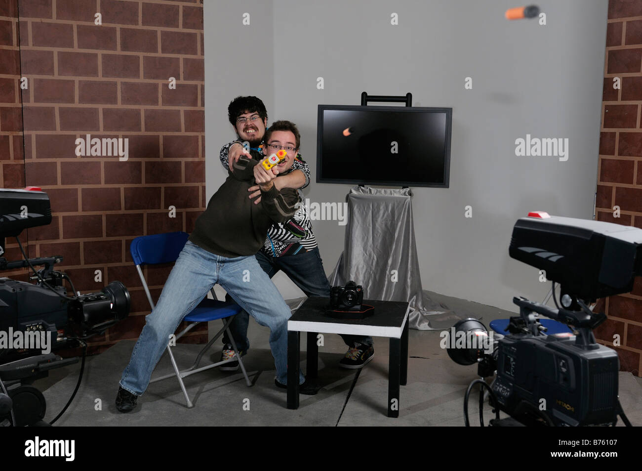Akteure auf der Bühne ein TV-Studio set mit Host versucht, Berserker Gast Spielzeug Pistole schießen zu kontrollieren Stockfoto