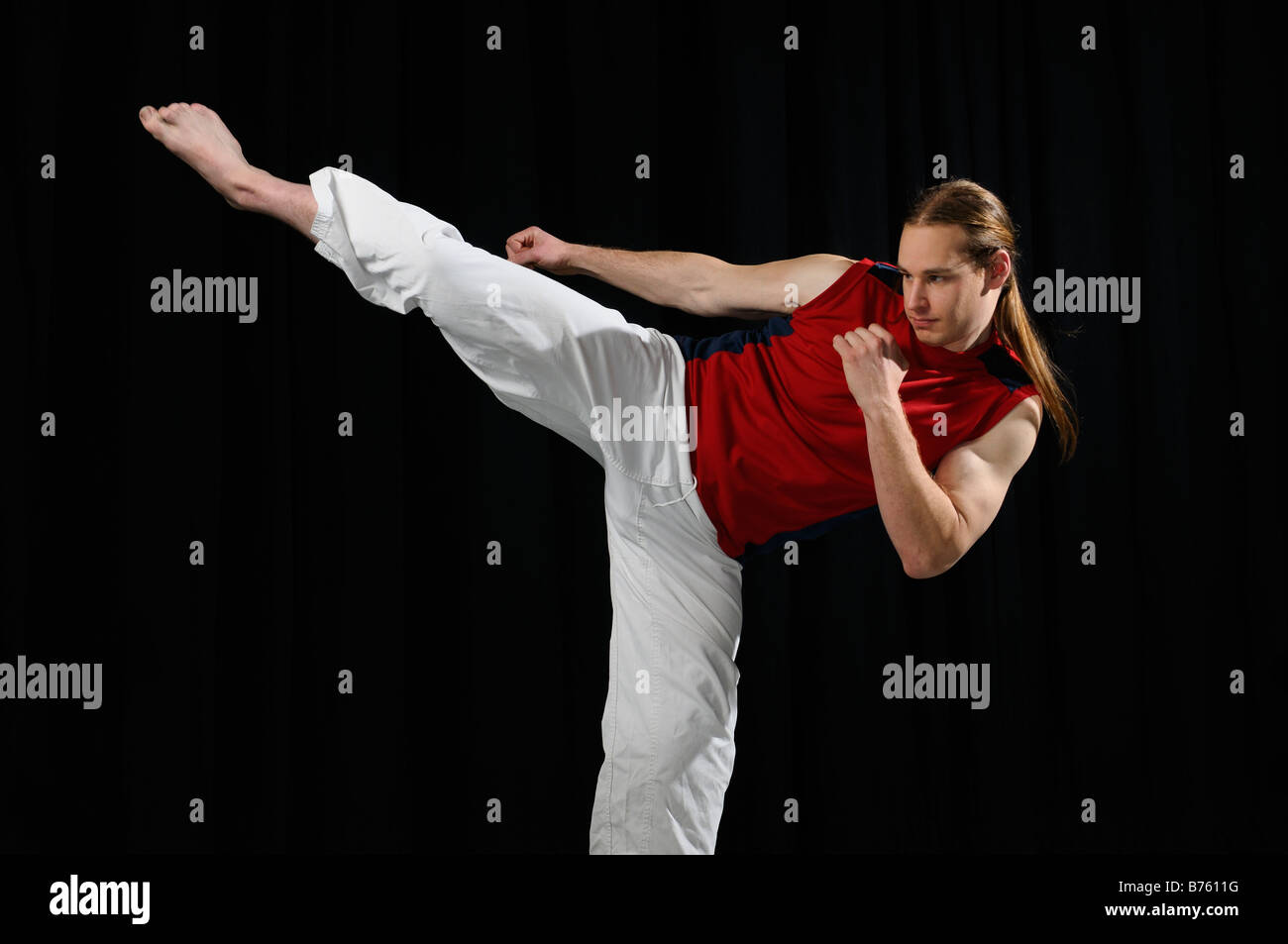 Männliche Karate Kämpfer wirft eine Seite vor einem schwarzen Vorhang kick Stockfoto