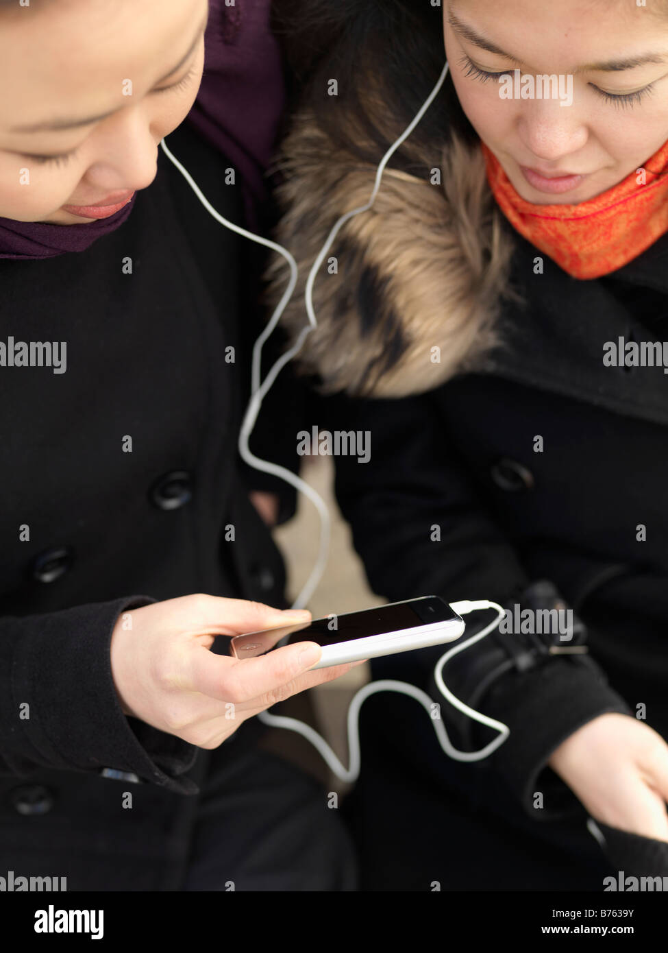 Zwei junge Frau Anteil Kopfhörer beim Musikhören auf einem Smartphone. Stockfoto