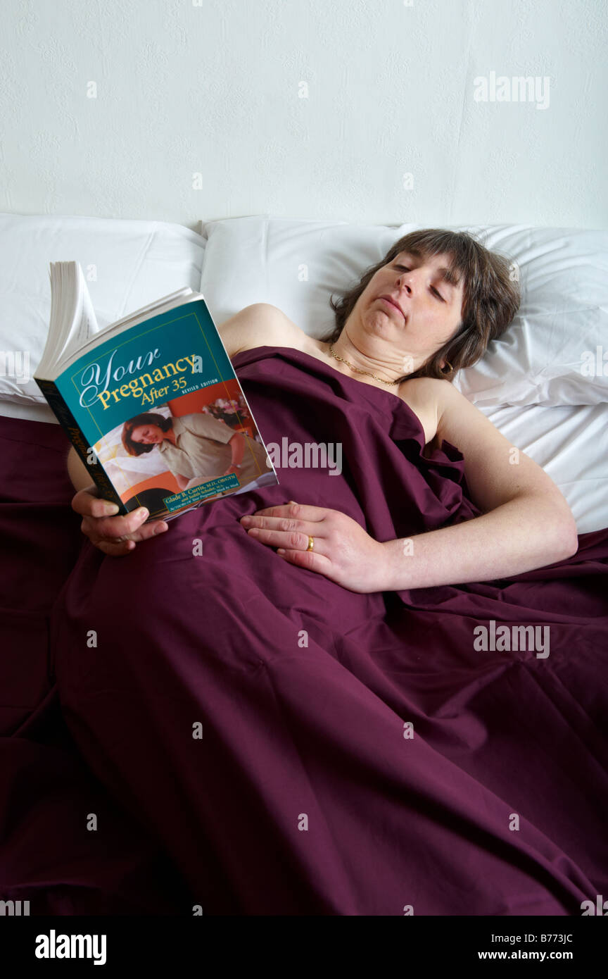 Applying Frau im Bett und las ein Buch über Schwangerschaft Stockfoto