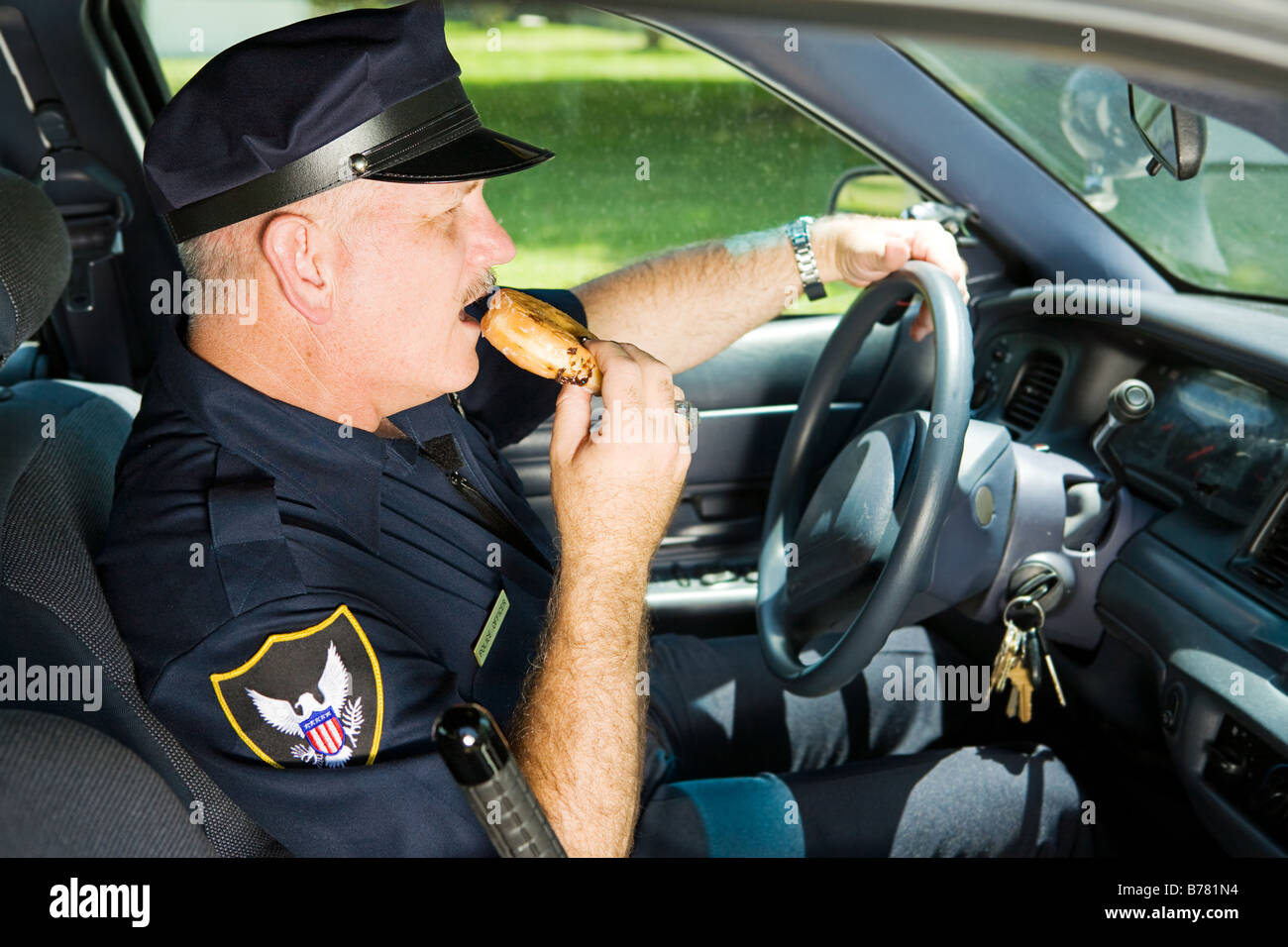 Polizist Naschen auf einen Donut sitzend in seinem Streifenwagen Stockfoto