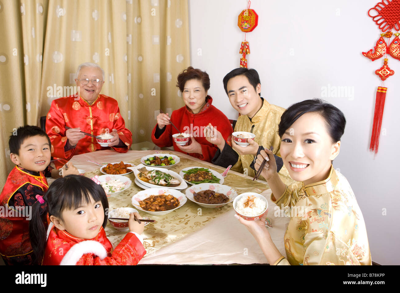 Familienmitglieder in traditioneller Kleidung mit Abendessen zusammen und lächelt in die Kamera Stockfoto
