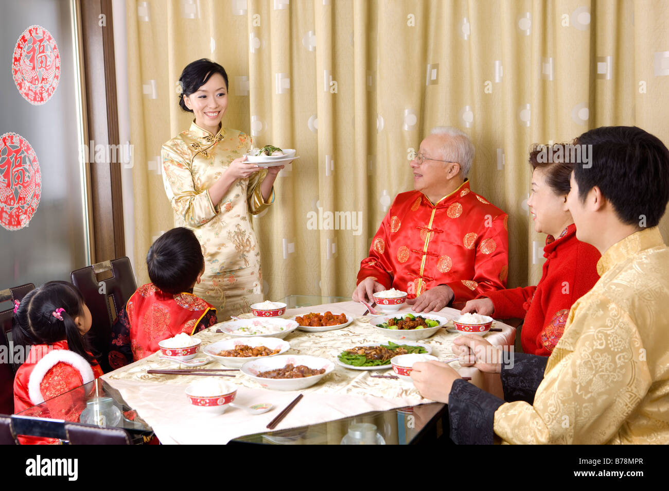 Familienmitglieder in traditioneller Kleidung mit Abendessen zusammen und mit Blick auf junge Frau Stockfoto