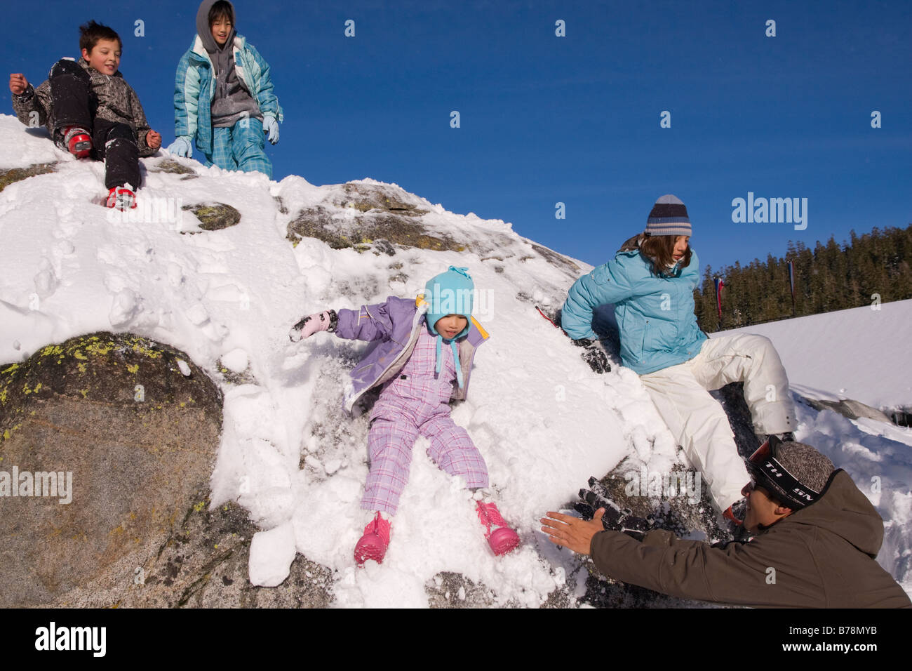 Vier Kinder rutschen einem schneebedeckten Felsen an Sierra at Tahoe ski Resort in der Nähe von Lake Tahoe in Kalifornien Stockfoto
