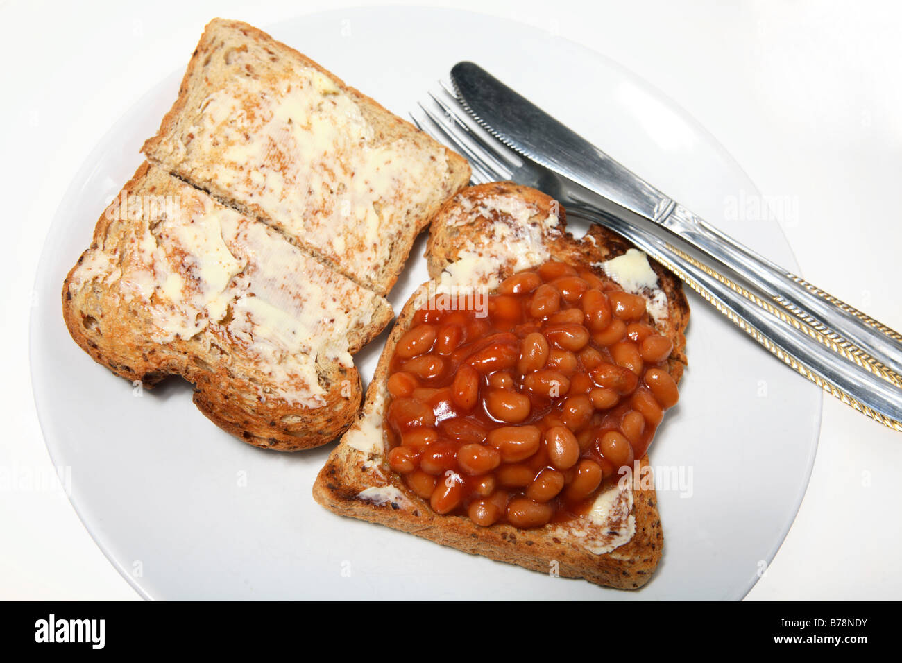 Bohnen auf Buttertoast mit einem Messer und Gabel - eine billige, tägliche Mahlzeit Stockfoto