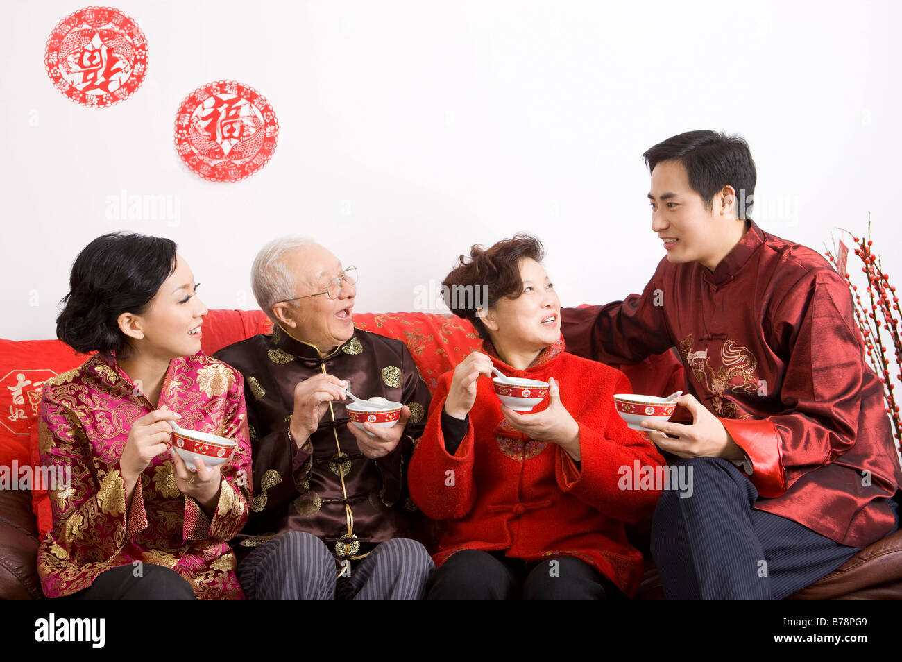 Familienmitglieder in der traditionellen Kleidung hält eine Schüssel geben und auf dem Sofa sitzen Stockfoto