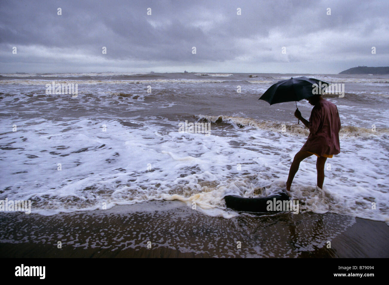 "Goa, Indien. Bei den Touristen gegangen, ein Beachcomber reinigt den leeren Strand im Regen. " Stockfoto