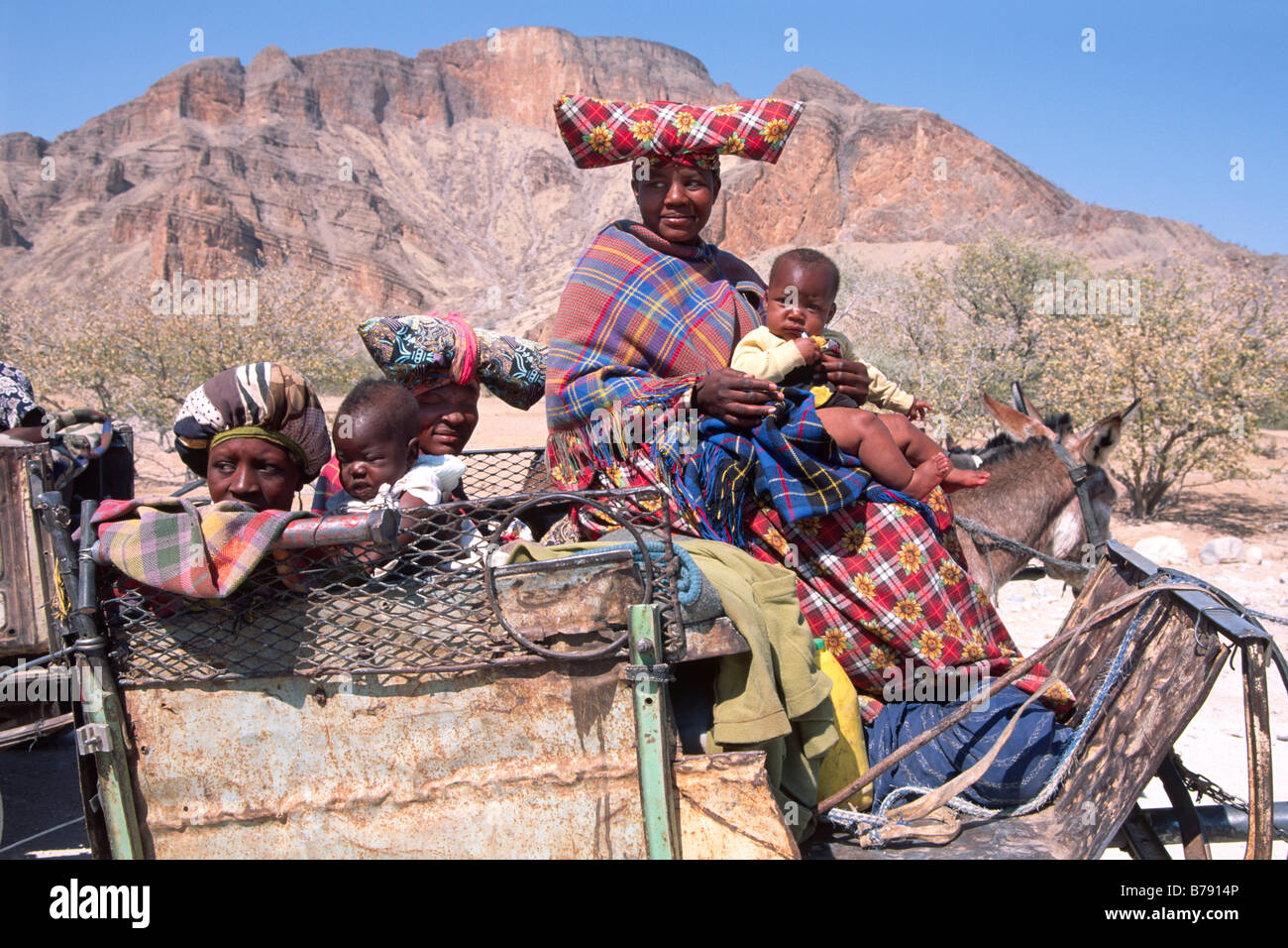 Herero Frauen in charakteristische Kleidung mit Babys auf einem Esel Warenkorb, Sesfontein, Kaokoveld, Namibia, Afrika Stockfoto