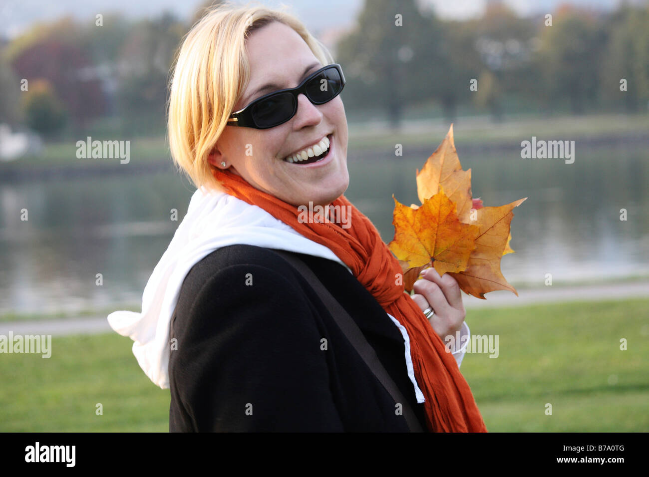 Frau trägt Sonnenbrille und hält herbstliche Blätter Stockfoto