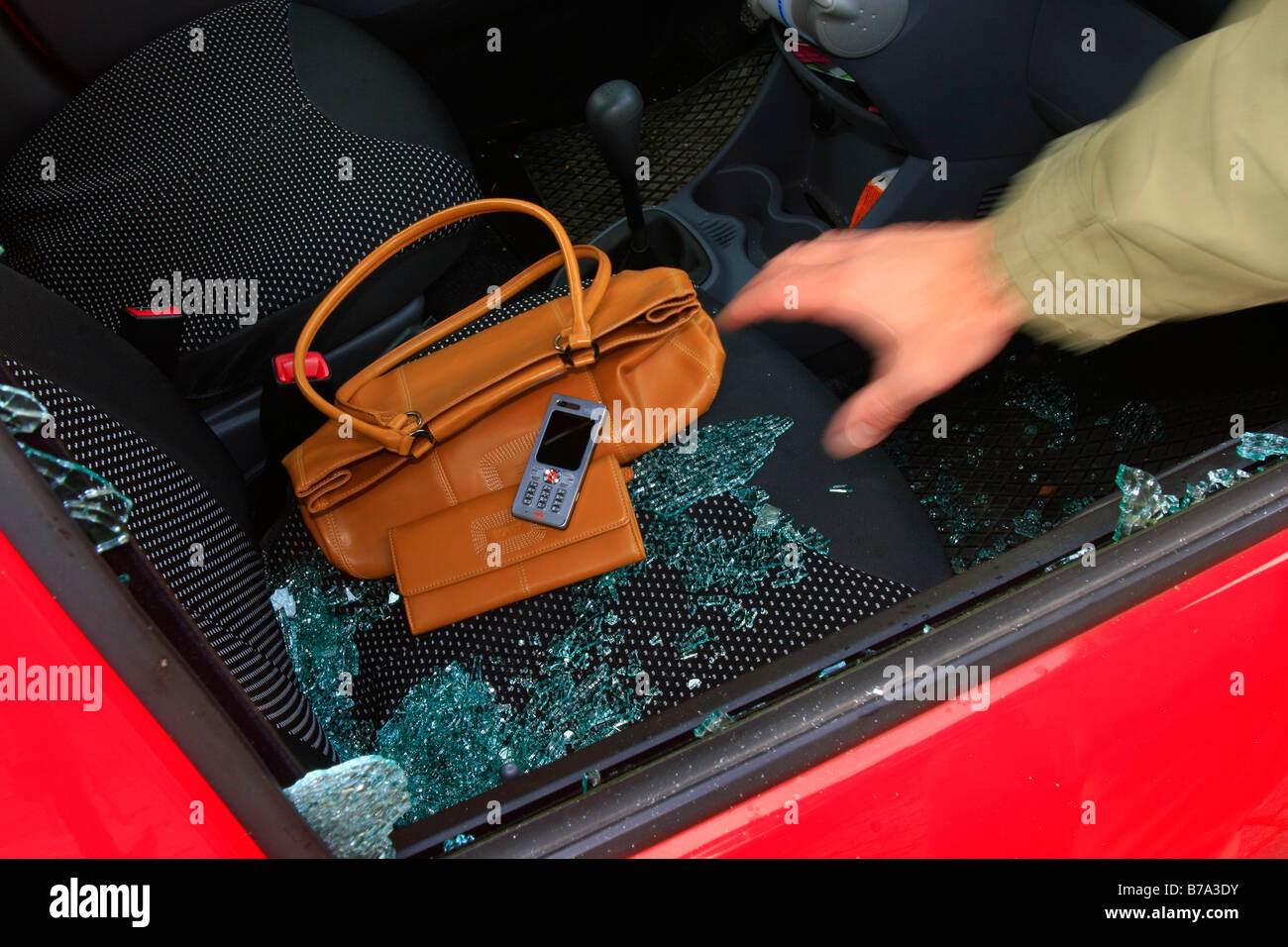 Auto-Einbruch, Hand greift durch das Seitenfenster an Wertsachen, d.h. Handtasche, Geldbörse und Handy Stockfoto