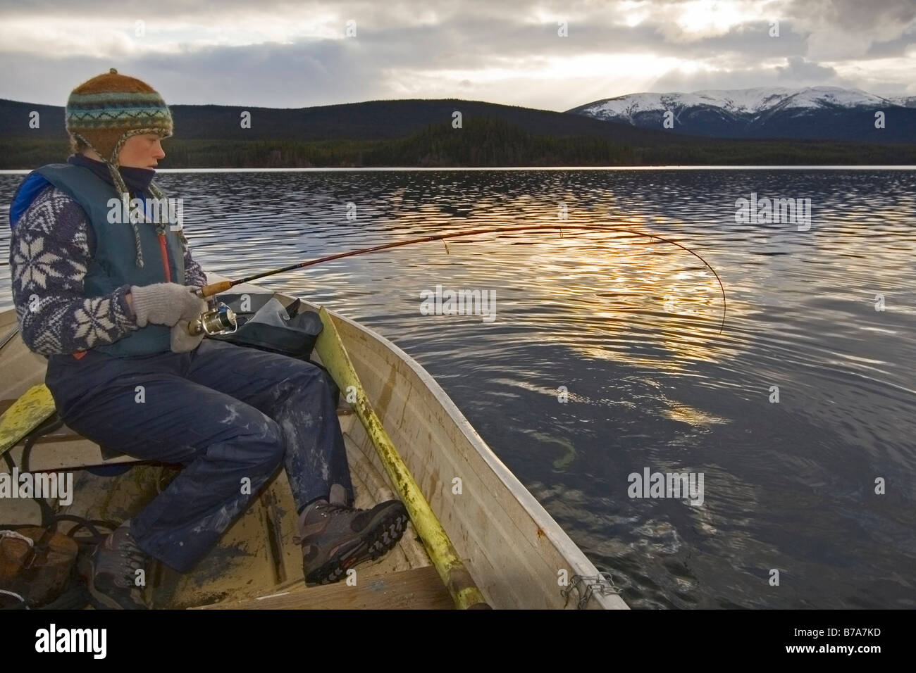 Frau in einem Boot kämpfen mit einen dicken Fisch an der Linie, Sonne gesetzt, Big Salmon Lake, Yukon Territorium, Kanada, Nordamerika Stockfoto