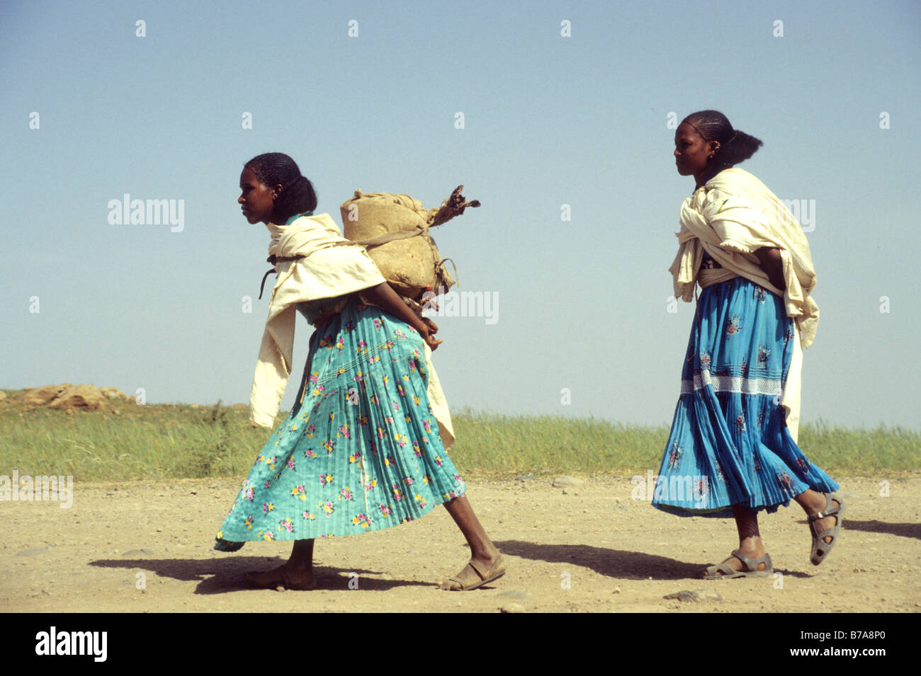 Zwei Oromo Frauen eine staubige Straße entlang, trägt man ein Bündel auf den Rücken geschnallt Stockfoto