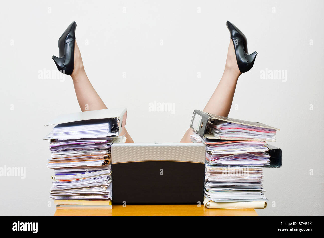 Beine für eine überarbeitete Geschäftsfrau ragte in die Luft hinter einem Schreibtisch mit Dateien geladen Stockfoto