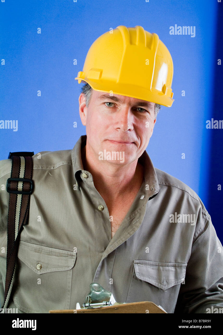 Ein Mann in einen Schutzhelm mit etwas hängt an seiner Schulter und ein Klemmbrett in der hand Stockfoto