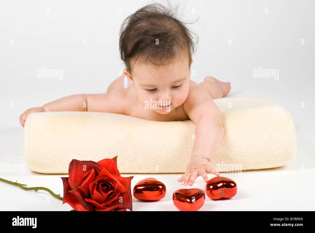 Ein süßes kleines Baby Mädchen erreichen für eine Rose und ein Herz geformt ornamets Stockfoto