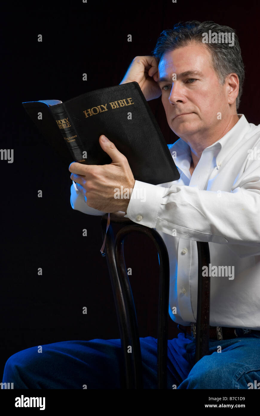 Ein Mann sitzt in einem dunklen Raum lesen eine Bibel Seite beleuchtet mit blauen Gel für Stimmung Stockfoto