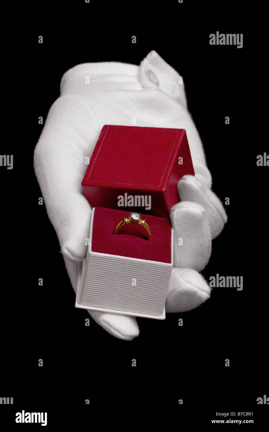 Hand, tragen einen weißen Handschuh, einen Diamant-Ring in einen Vorschlag der Ehe isoliert auf einem schwarzen Hintergrund zu präsentieren Stockfoto