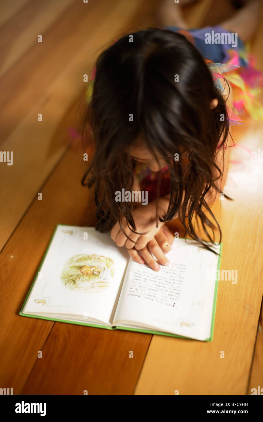 Fünf Jahre altes Mädchen Lügen Erdgeschoss Beatrix-Potter-Buch lesen Stockfoto