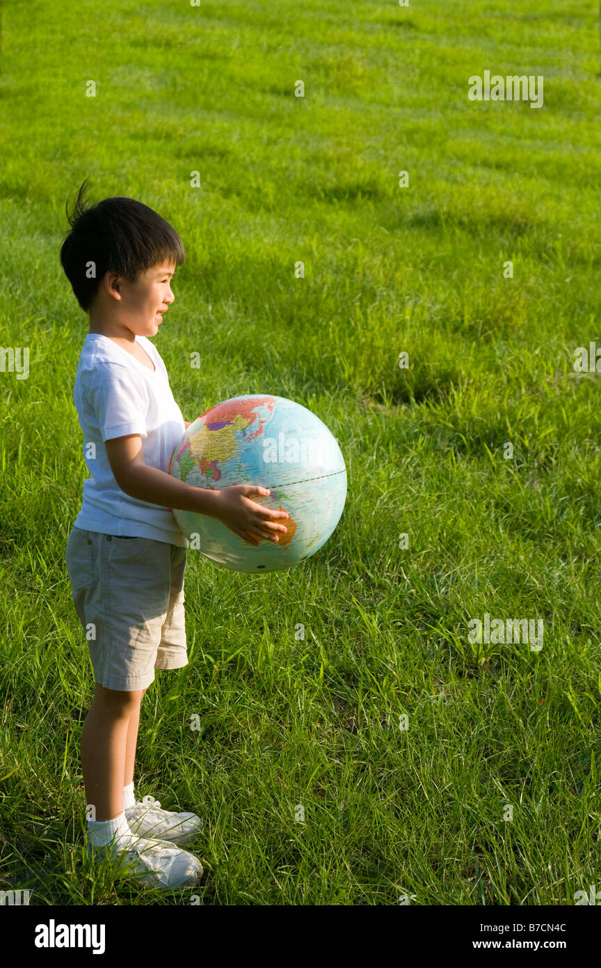 Kleiner Junge hält einen Globus auf dem Rasen und wegsehen Stockfoto