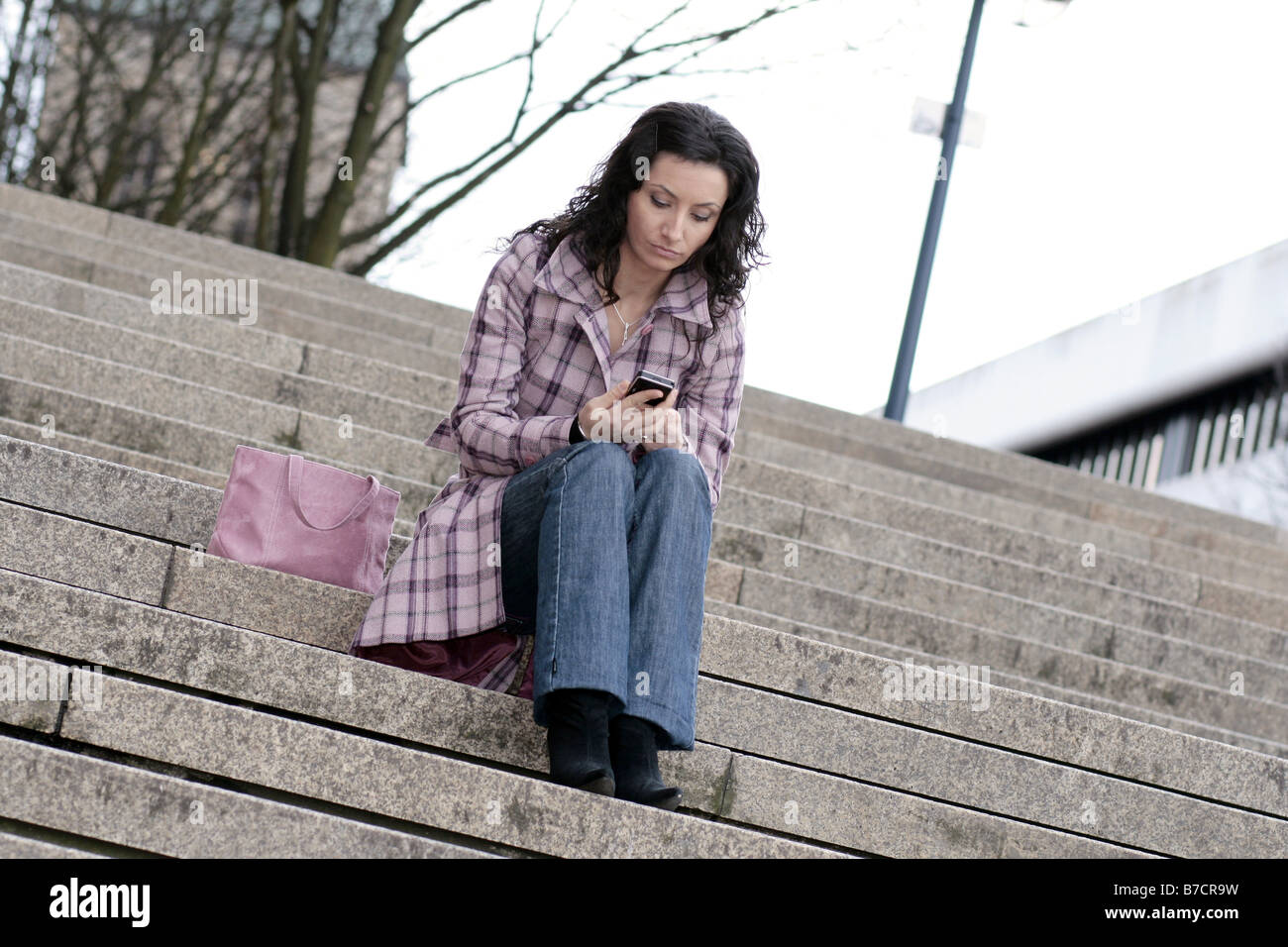 junge Darkhaired Frau sitzt auf der Treppe, Blick auf ihr Handy Stockfoto