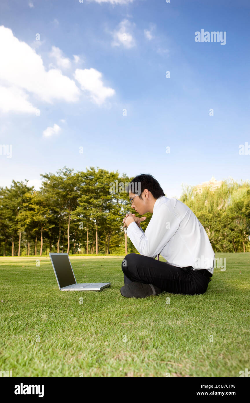 Ein Geschäftsmann auf Rasen sitzen und mit Blick auf den laptop Stockfoto