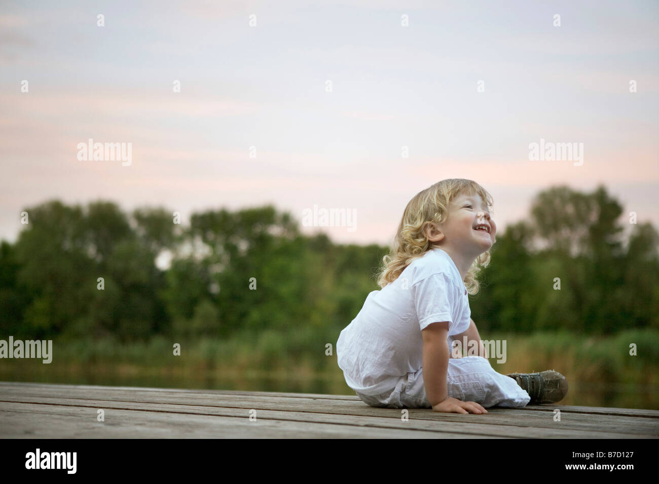 Ein lachender Junge sitzt auf einem Steg Stockfoto