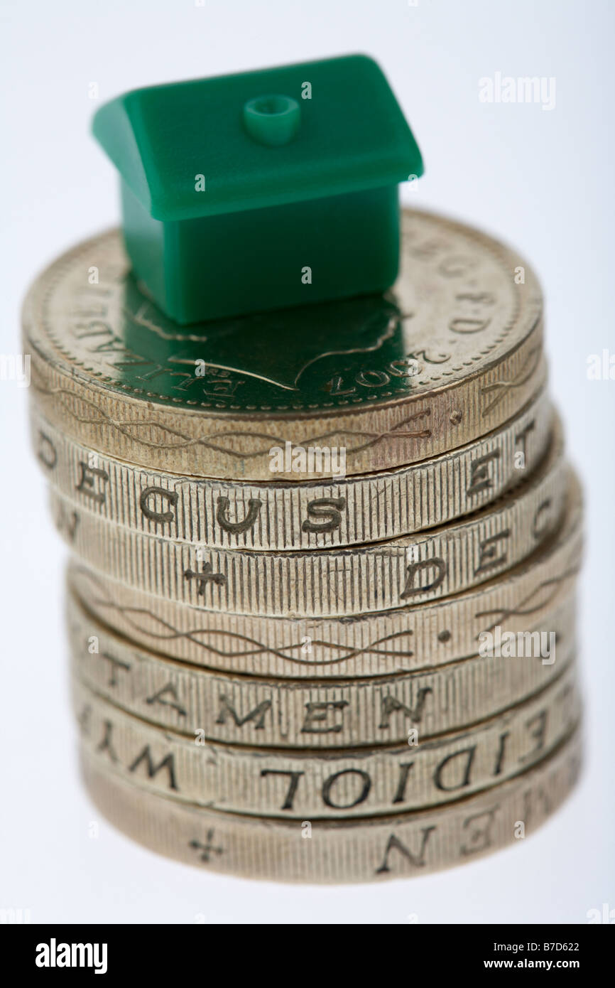 kleines Spielzeug Haus sitzt auf einem Stapel von gebrauchten Pfund-Münzen auf weißem Hintergrund Stockfoto