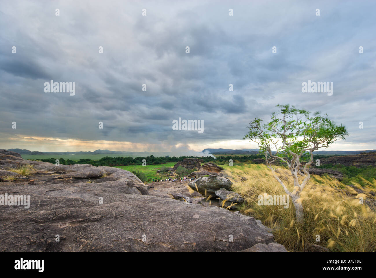 Touristen sitzen auf den Felsen des Ubirr mit einem Feuer im Hintergrund im Kakadu National Park Stockfoto