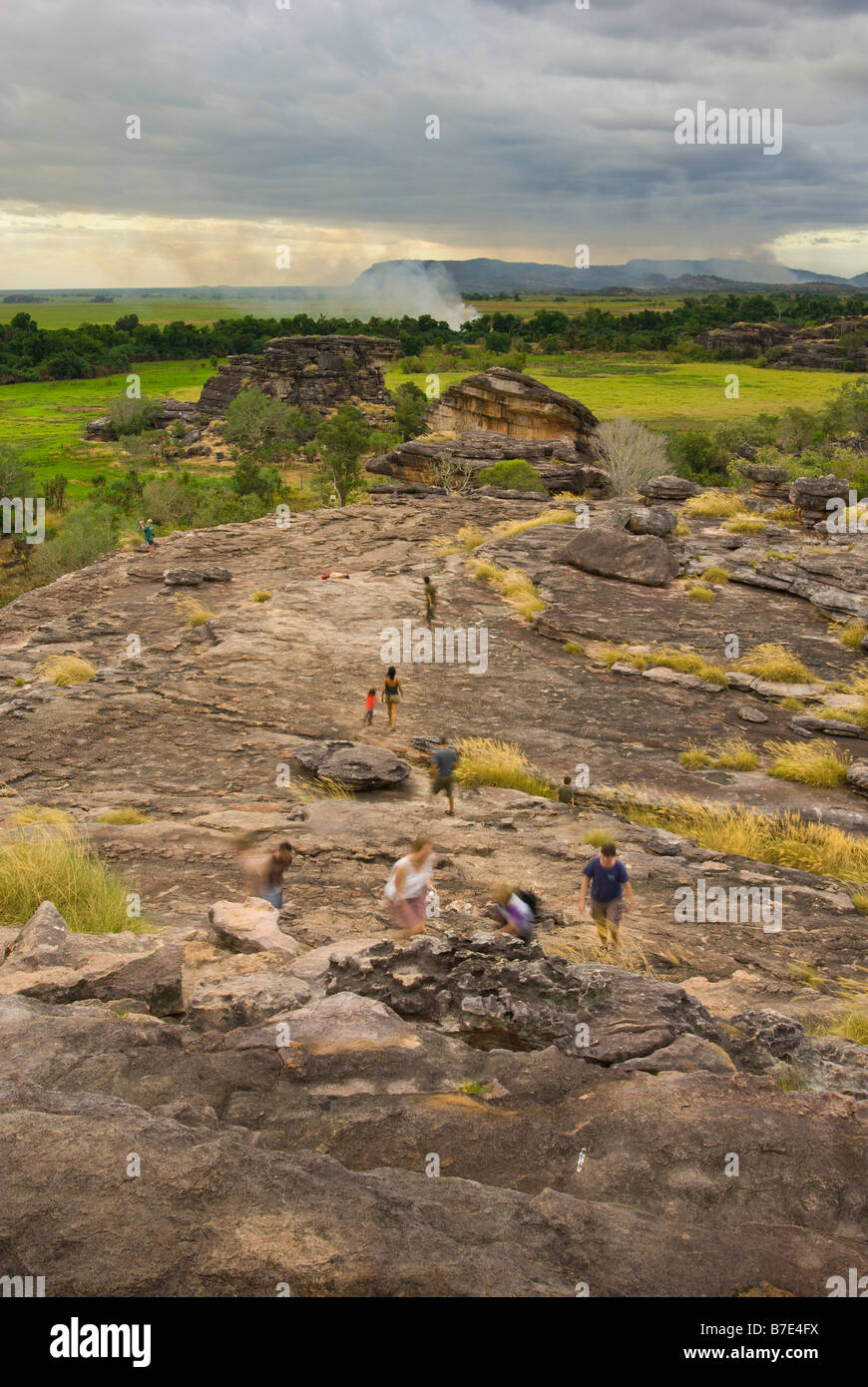 Touristen zu Fuß über die Felsen des Ubirr mit einem Feuer im Hintergrund im Kakadu National Park Stockfoto