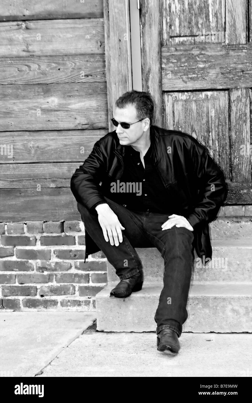 Mann in schwarzem Ledermantel sitzt vor einer Tür wartet auf seine Datum ankommen Stockfoto